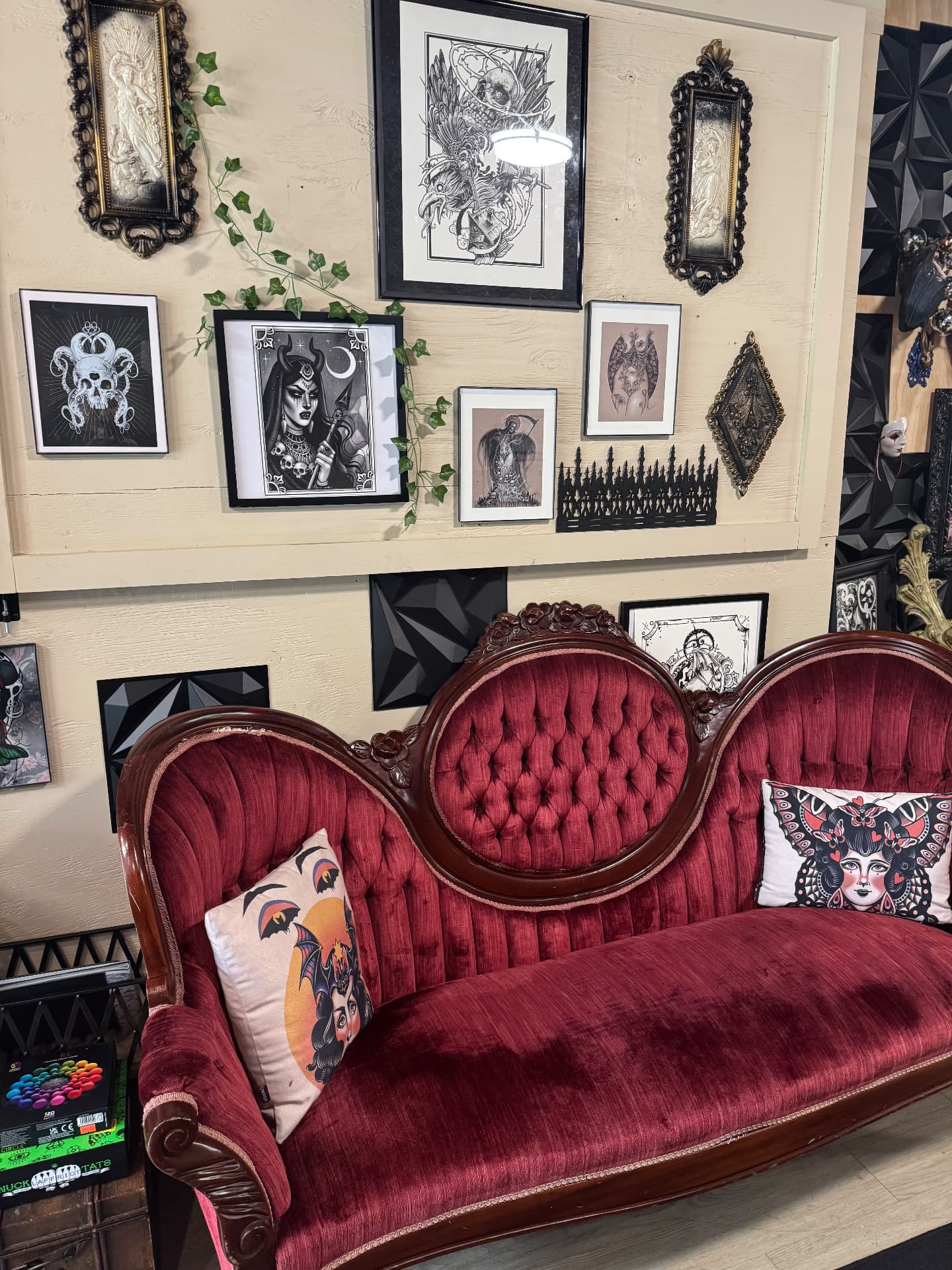 Salon-style gallery wall of framed tattoo flash above a red velvet Victorian sofa