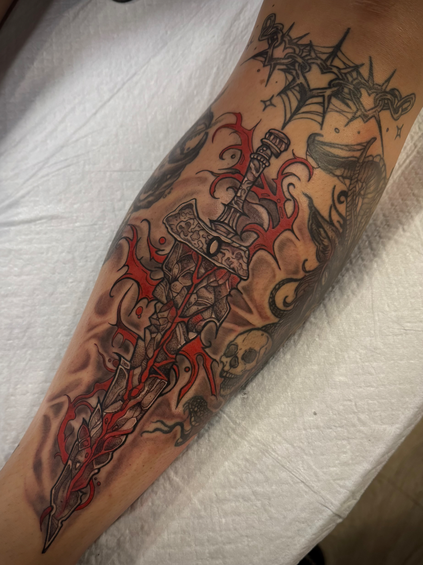 Shattered stone greatsword forearm tattoo with bold red thorned flourishes, skull and serpent