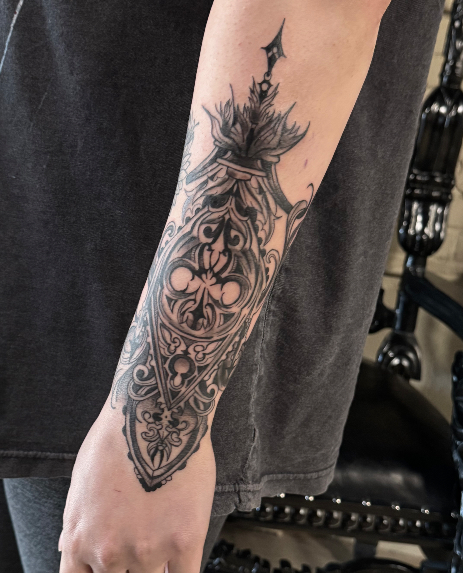 Ornamental blackwork forearm piece shaped like a gothic reliquary with quatrefoil tracery, filigree scrolls and a flaming finial