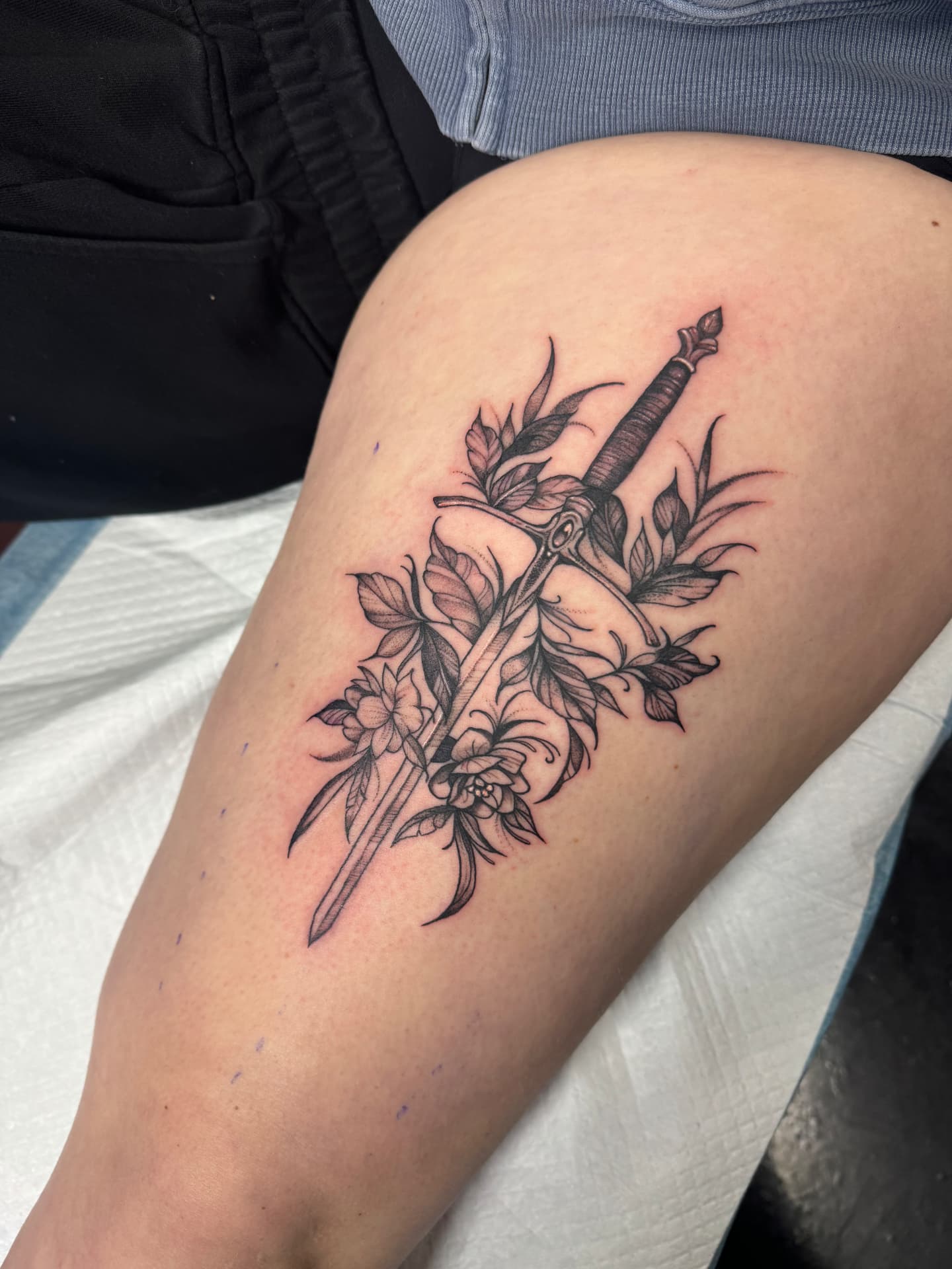 Fine line dagger and florals thigh tattoo in soft black and grey